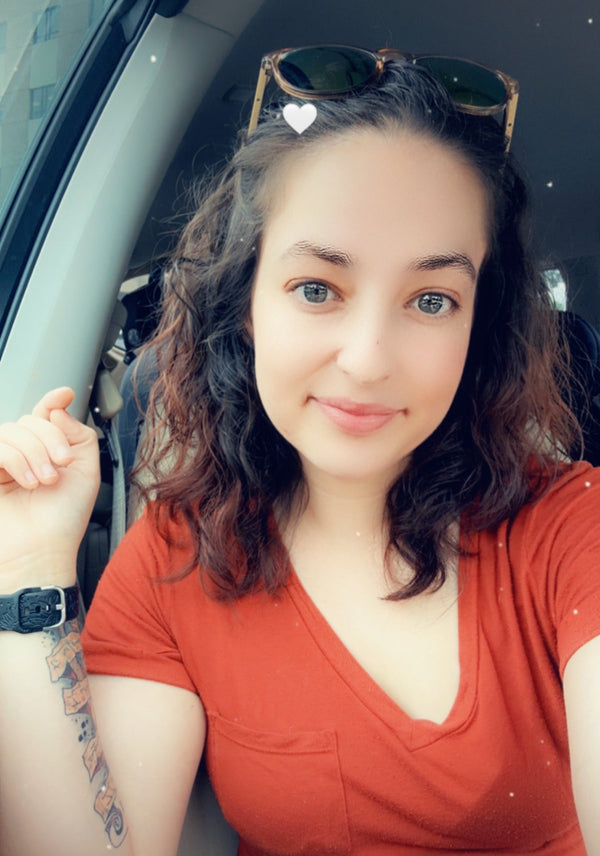 Woman in a red shirt sitting inside a vehicle with sunglasses on her head.